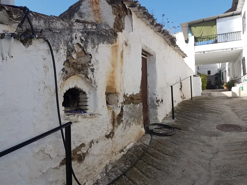 Callejón empedrado entre casas encaladas con un horno de pared y la cal desconchada