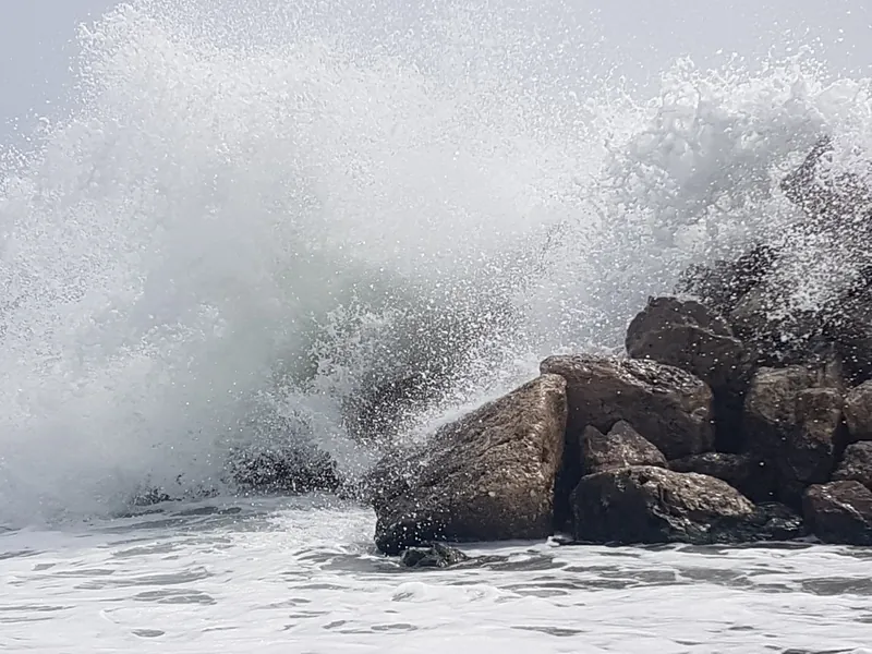 Ola rompiendo contra unas rocas y levantando una gran cortina de espuma