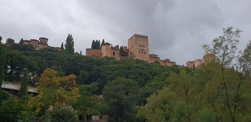 La Alhambra sobre una colina rodeada de árboles bajo un cielo nublado