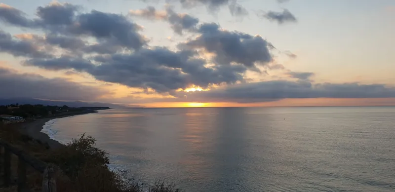 Amplia vista de la costa al amanecer con nubes iluminadas y el mar en calma
