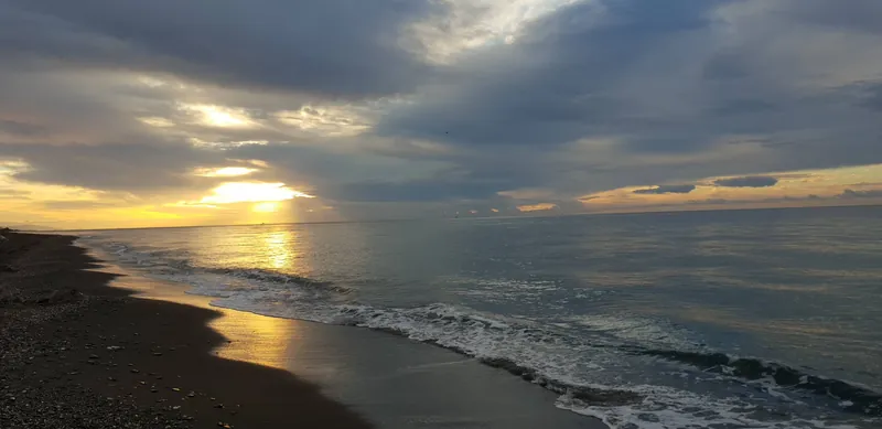 Cielo cargado de nubes con rayos de sol sobre una playa y el mar