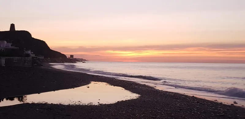 Playa de cantos con una charca que refleja el cielo rosado del amanecer