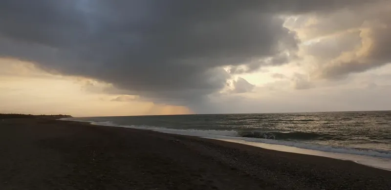 Nubes de tormenta sobre una playa con una cortina de lluvia en el horizonte