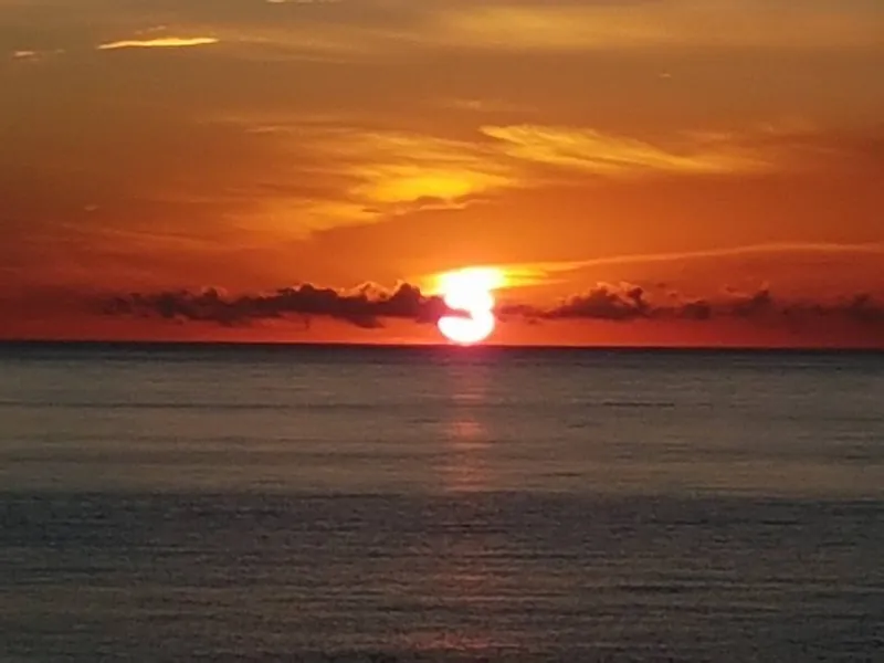 Sol rojo sobre el horizonte con el cielo naranja y nubes alargadas