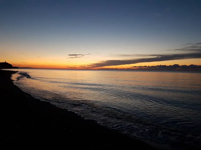 Playa oscura al anochecer con un último resplandor naranja en el horizonte