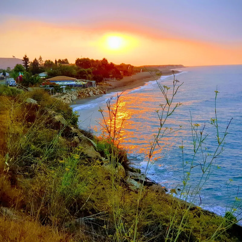 Sol sobre el mar al atardecer con la costa y una playa con chiringuito
