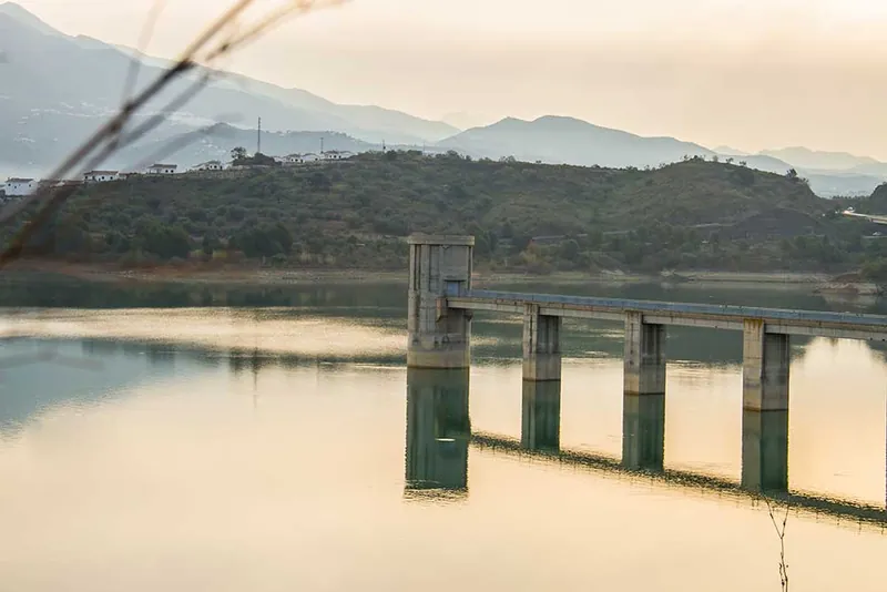 Torre de toma de agua y pasarela sobre un embalse con montañas al fondo
